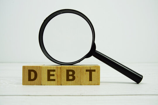 DEBT alphabet letters with magnifying glass on wooden background