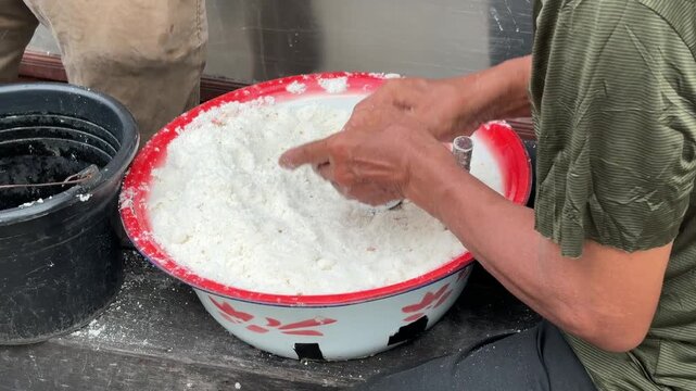 An Asian man selling traditional food fills a bamboo mold with Putu cake batter made from rice flour and palm sugar before the steaming process begins.