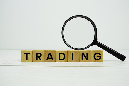 TRADING alphabet letters with magnifying glass on wooden background