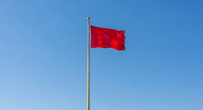 Bright red flag waving on a tall flagpole against a clear blue sky background