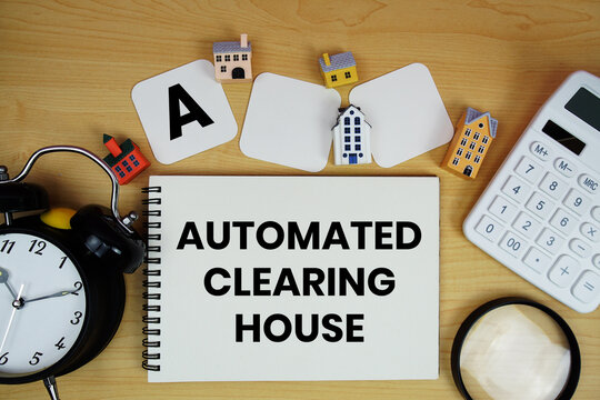 ACH Automated Clearing House text written on notepad with house model, alarm clock and magnifying glass on wooden background