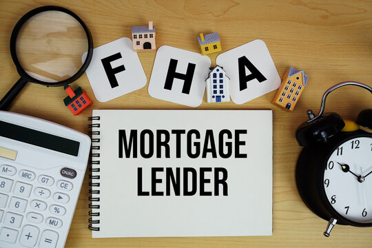 FHA Mortgage Lender text written on notepad with house model, alarm clock and magnifying glass on wooden background