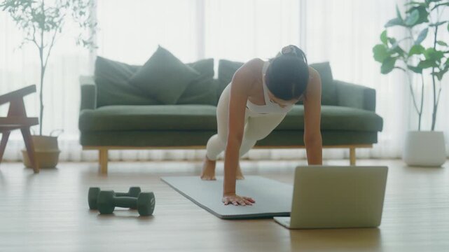 Young Asian woman doing sport exercises indoor. Beautiful girl workout at home. Athletic outfit is doing mountain climber exercises