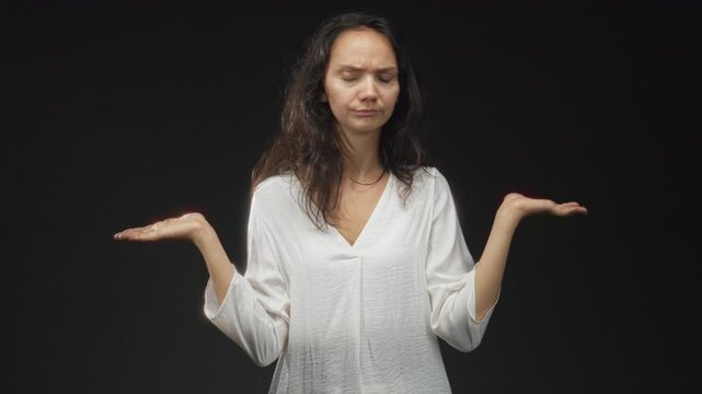Woman holds palms up in a questioning shrug, palms visible and pensive expression in studio; uncertainty decision.