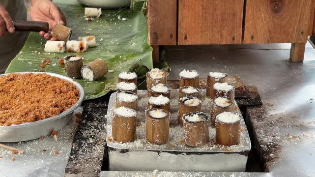 An Asian man selling traditional food removes freshly steamed putu cake dough from a bamboo mold after cooking during the street food preparation process.