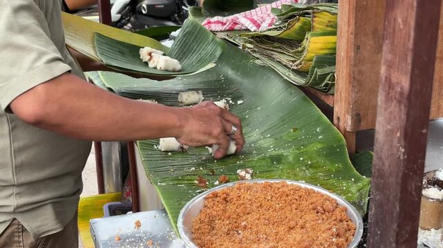 An Asian man selling traditional food wraps freshly cooked putu cake to be served or sold as a traditional Indonesian street food snack.