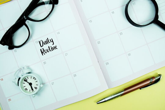 Daily Routine message written on calendar date with alarm clock, glasses and magnifying glass on yellow background