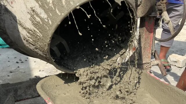 Closeup of a cement mixer machine pouring wet concrete into a bucket at a construction site