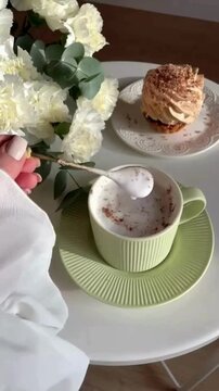 Female Hand Stirring Coffee and Creamer in Cup with Small Spoon in Cozy Morning Atmosphere