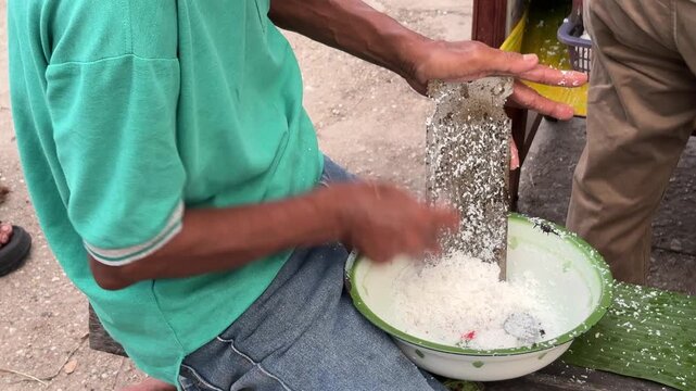 An Asian man is doing the activity of manually grating coconut.