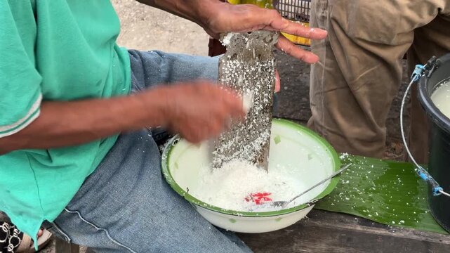 An Asian man is doing the activity of manually grating coconut.