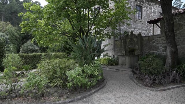 View of stone house garden with fountain trees plants and curved cobblestone pathway
