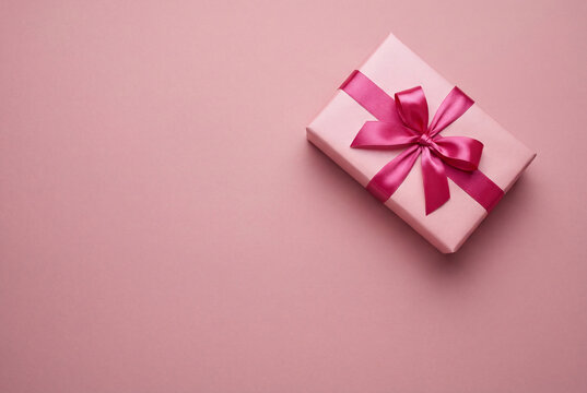 Pink gift box with a vibrant fuchsia satin ribbon bow viewed from above on a pink surface