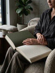 Obraz premium Hands holding an open, hardcover book with blank pages, seated in a comfortable chair