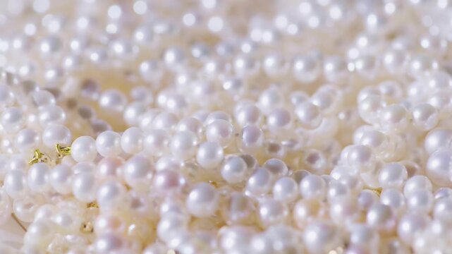 Close up slow motion footage of lustrous white pearls tumbling and scattering creating a luxurious and elegant textured background.