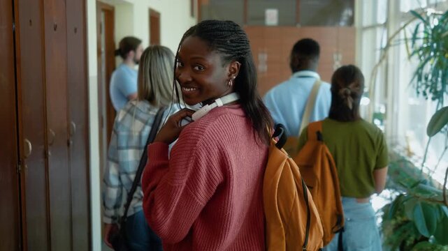 Tracking shot from behind of diverse university students walking through hallway as smiling Black female student turns and looks at camera.