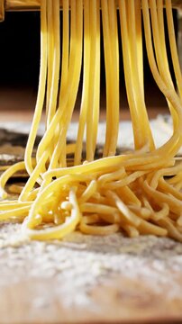 Close-up of fresh spaghetti being extruded from a pasta maker machine onto a floured surface