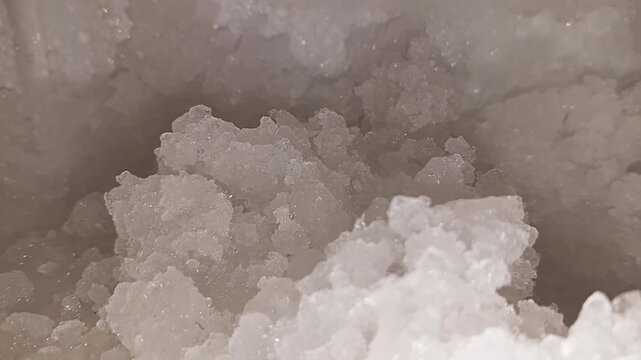 Macro close up view of fresh white ice crystals showing detailed texture and patterns forming on the surface of a frozen block of cold water