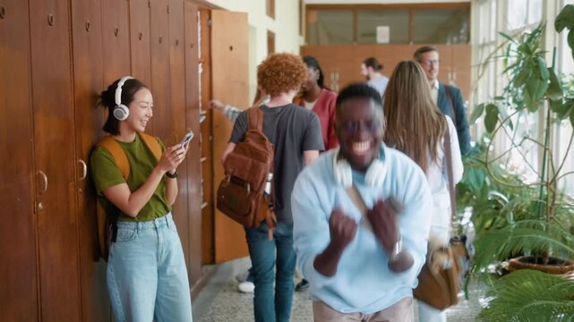 Happy African college student reacts to passing exam or receiving good academic results on smartphone in university hallway with classmates.