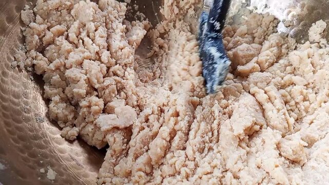 A hand uses a black kitchen spatula to mix thick dough inside a shiny hammered copper bowl while preparing a delicious traditional homemade dessert recipe today