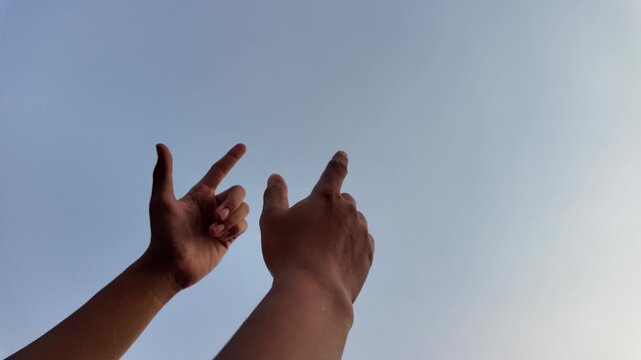 A dynamic shot of two hands forming finger gun gestures and "shooting" upward toward a vast, clear blue sky. This playful or assertive motion captures a sense of energy, targeting goals, or lightheart
