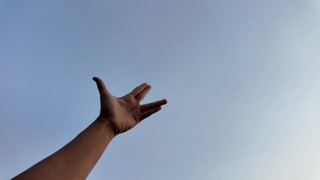 A close-up shot of a hand performing the iconic Vulcan salute gesture, with fingers parted between the middle and ring finger, set against a bright and clear blue sky.