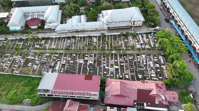 A view from above of an urban cemetery with rows of graves and headstones nestled among the buildings.