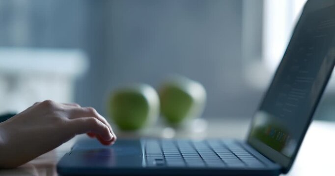 Teen's hands  talking, pressing keys and using the touchpad during online learning and communication. Blurred kitchen interior , apple