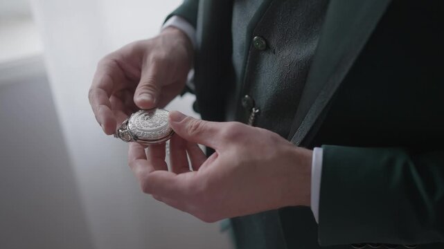 Close view of hands opening vintage pocket watch while dressed in formal attire