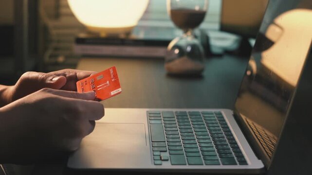 Slow Motion Close-up of Person Holding Credit Card in Front of Laptop, Hesitating and Thinking Before Online Purchase, Financial Decision Concept.