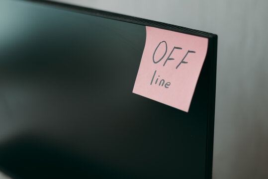 A sticky note reading OFF line is attached to the edge of a modern computer monitor in a workspace