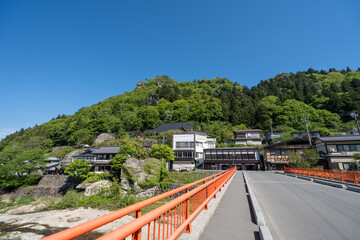 Obraz premium Orange Bridge Leading to Ryokan Inn Buildings at Base of Green Mountain at Yamadera