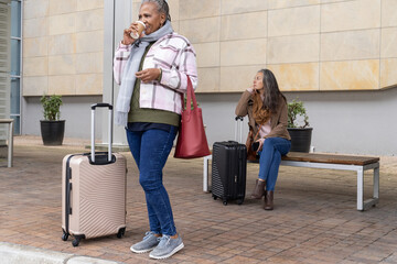Diverse female travelers waiting at forecourt, holding rolling suitcases and coffee cup, copy space © wavebreak3
