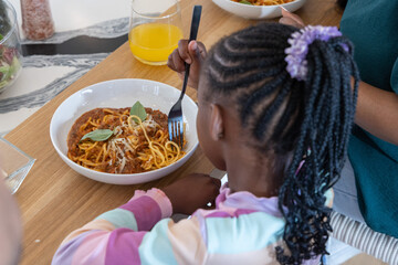 African American parent and child sharing spaghetti at home, girl wearing pastel sweater black fork © wavebreak3
