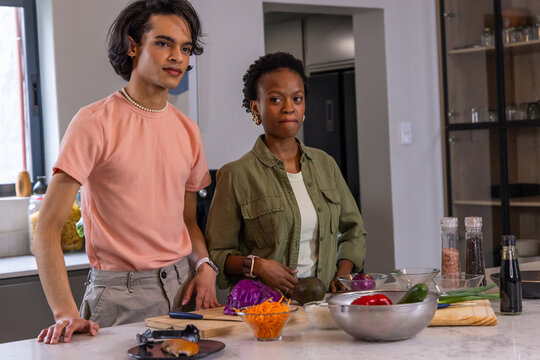 Diverse couple chopping vegetables and preparing salad at kitchen island with cutting board