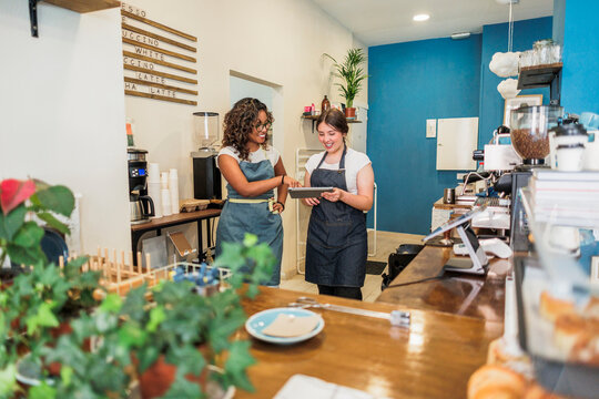 Diverse women baristas collaborating discussing business using tablet