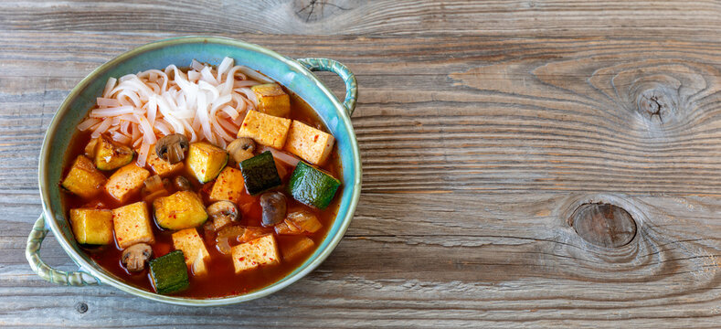 Vegan version of kimchi soup with tofu and rice noodles. Rustic wooden background - a banner with space for additional content. 