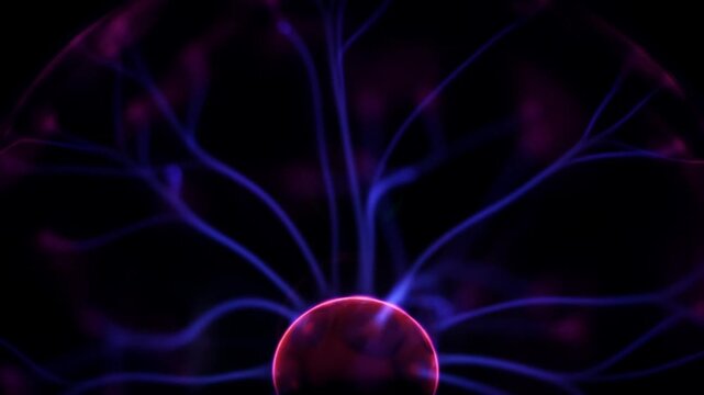 Close up of thin violet and blue electric tendrils moving like organic branches across a black background representing high voltage static discharge.