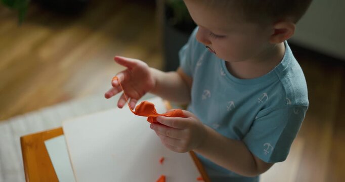 Slow motion of a cute playful child making shapes from orange play dough