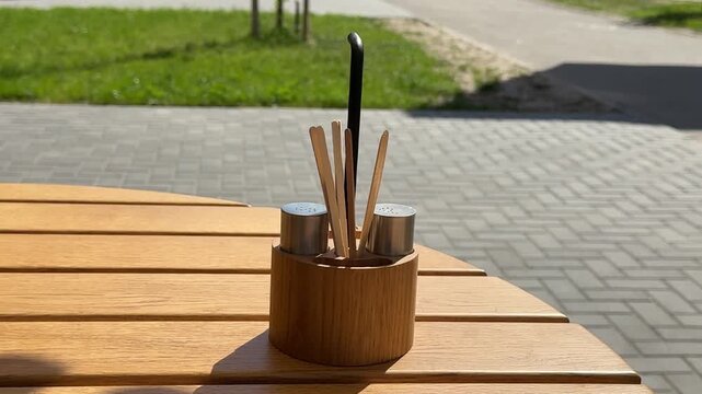 Woman taking white napkins from wooden table organizer with salt pepper and coffee stir sticks at outdoor cafe. cozy restaurant atmosphere with everyday dining details in warm sunlight. 