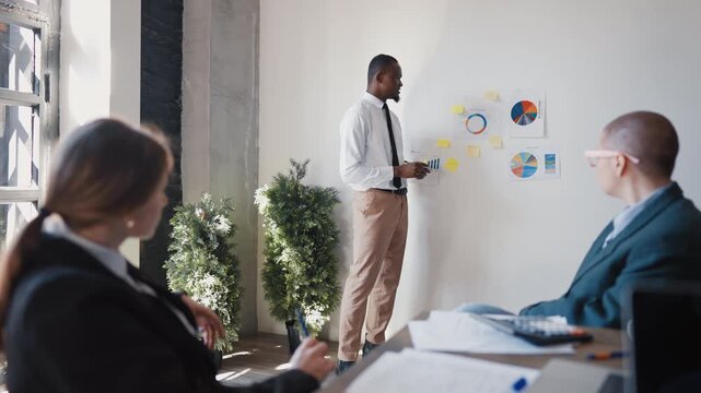 Business conference, african man presenting financial report for colleagues. Teamwork in international company, coworkers listening to presentation of startup owner, investments and economic risks