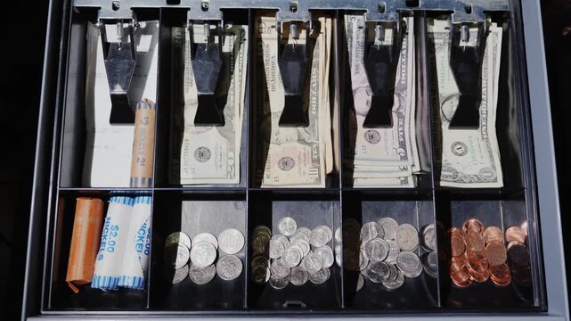 Cash drawer opens revealing variety of american currency including neatly organized bills and stacks of coins, motion footage showcasing financial transactions and money management.