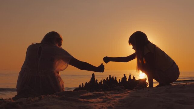 Mother and daughter building sandcastle on sandy beach during golden hour sunset backlit silhouette view peaceful coastal moment of family connection play and happiness by seaside scenery at summer 