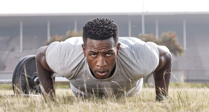Outdoor, fitness and black man with push up on grass for calisthenics, core exercise and portrait. Serious, training and athlete with endurance workout for strength challenge, stadium and muscle gain