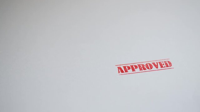 Rubber stamp marking white paper sheet with red ink text saying approved in close up view providing professional business document verification service for corporate finance administration work