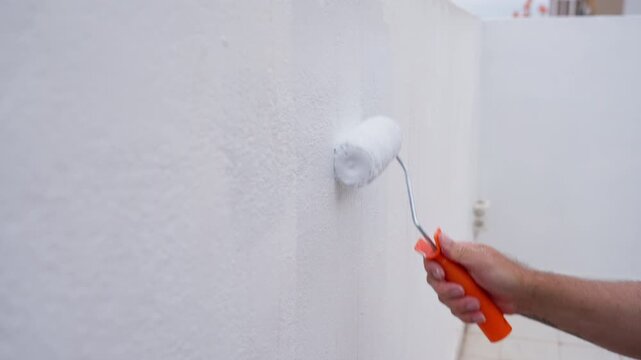 Close-up of a house painter's hand using a paint roller to apply white paint on a textured wall during home renovation, showing the diy concept of interior decorating