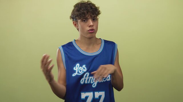 Teenage boy gesturing with hands while wearing blue los angeles basketball jersey in studio; thoughtful introspection youthful uncertainty.