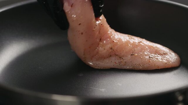 Slow motion man hand put chicken fillet on non stick pan closeup