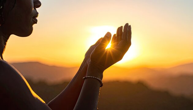 A silhouetted figure reaches towards a vibrant sunset, hands outstretched as if embracing the warmth and light of the fading day over a mountainous landscape.