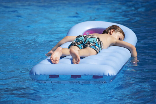 Boy in swimming trunks  lying face down on a lilo in a swimming pool